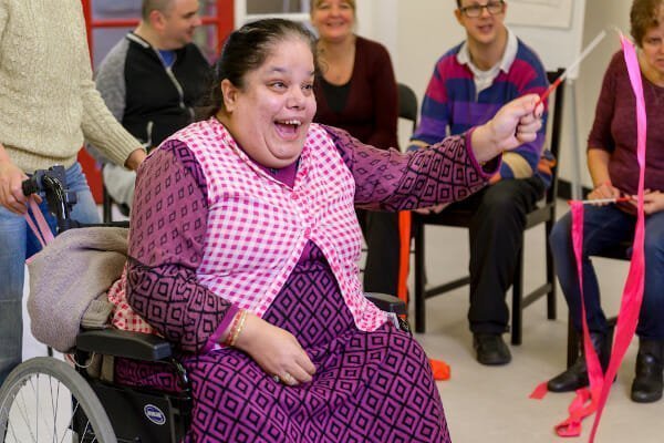 a woman in a pink dress smiles and waves a stick