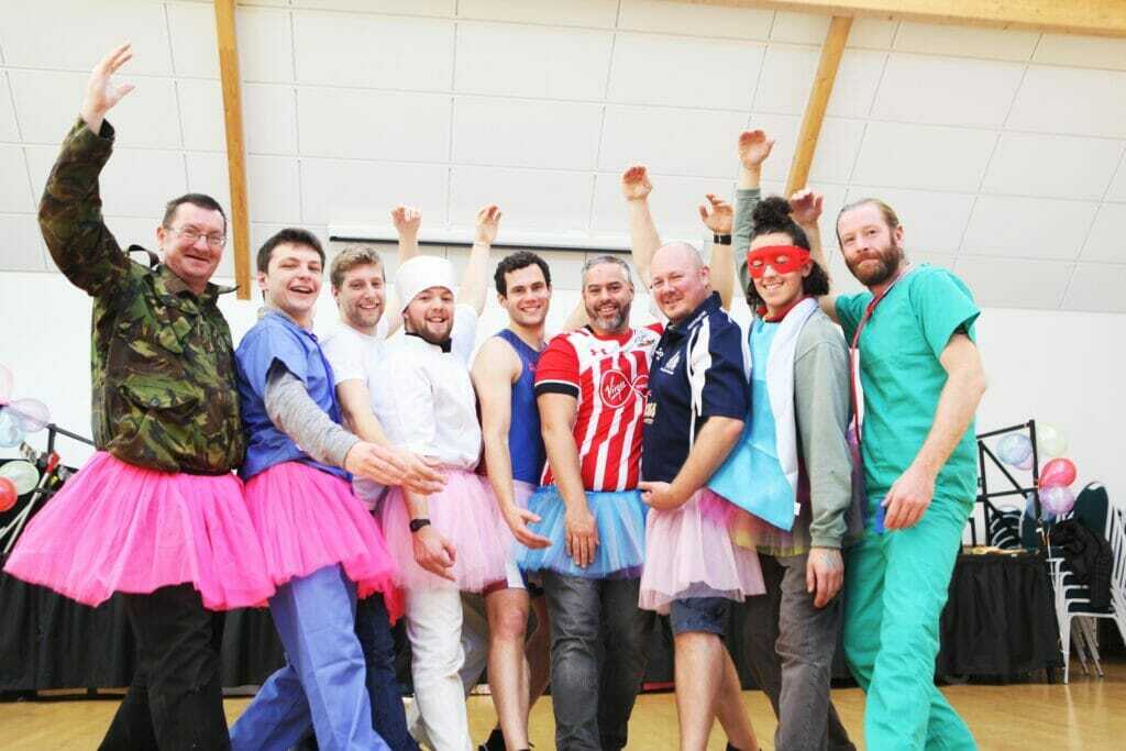 Group of dads pose in tutus and superhero outfits