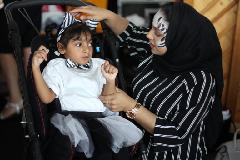 A dance helper with zebra face paint puts zebra ears on a child