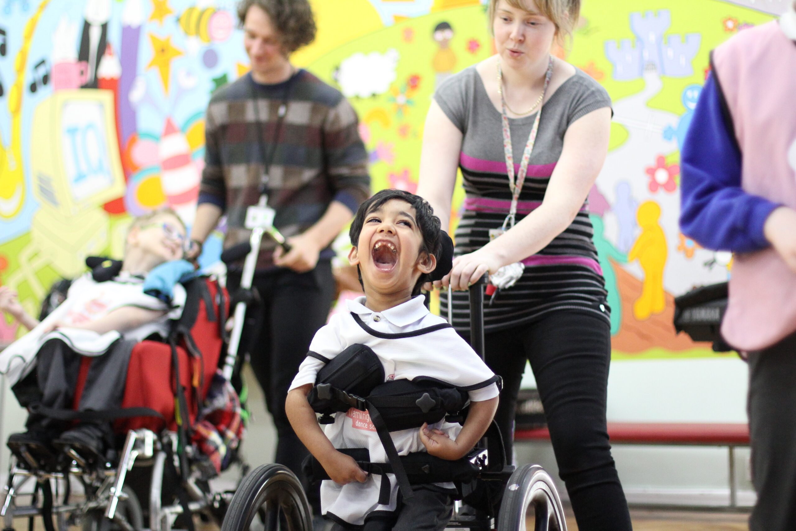 A young boy in a wheelchair gives a huge smile as he takes part in a Flamingo Chicks class, supported by his learning assistant