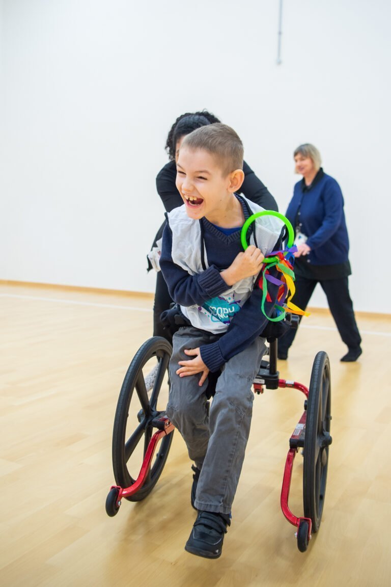 A boy in a wheelchair smiles and plays with a ribbon ring